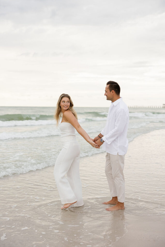 Stylish couple in coordinated beach engagement photo outfits by the shoreline