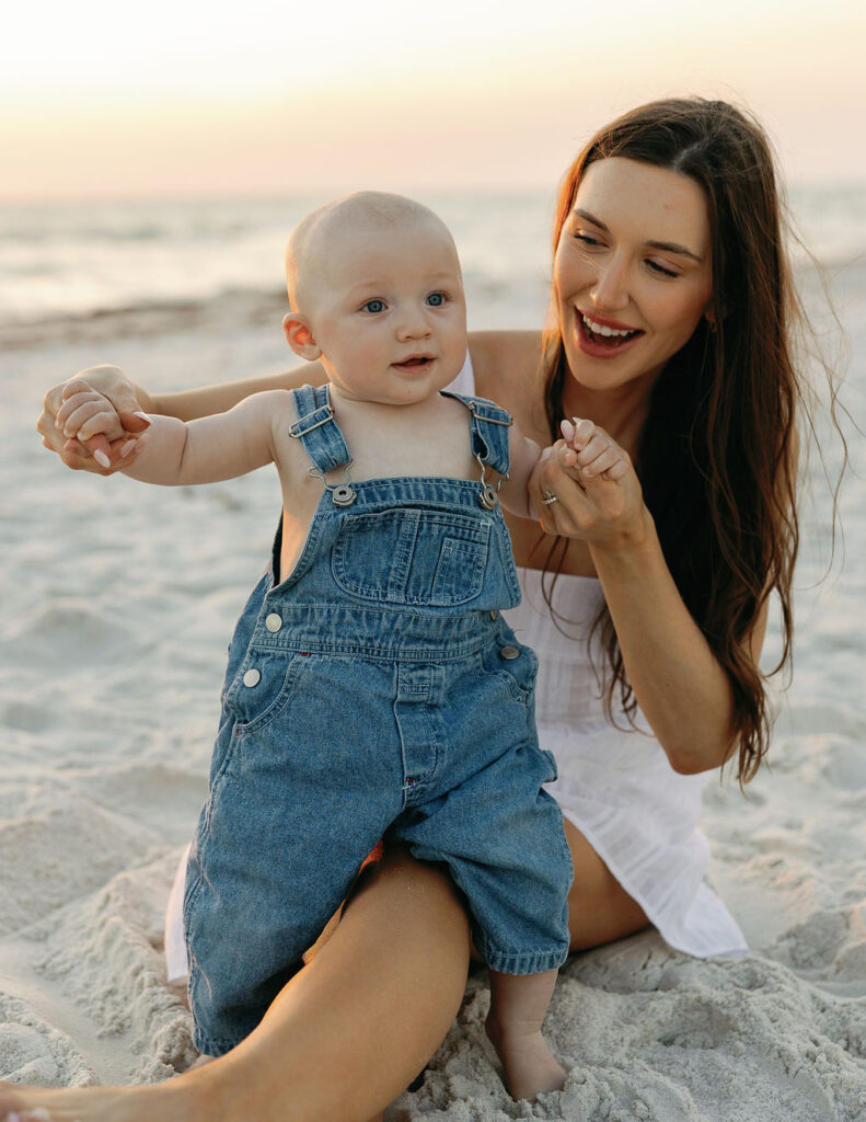 Mom with baby dressed in overalls on beach with ideas for what to wear for family beach photos