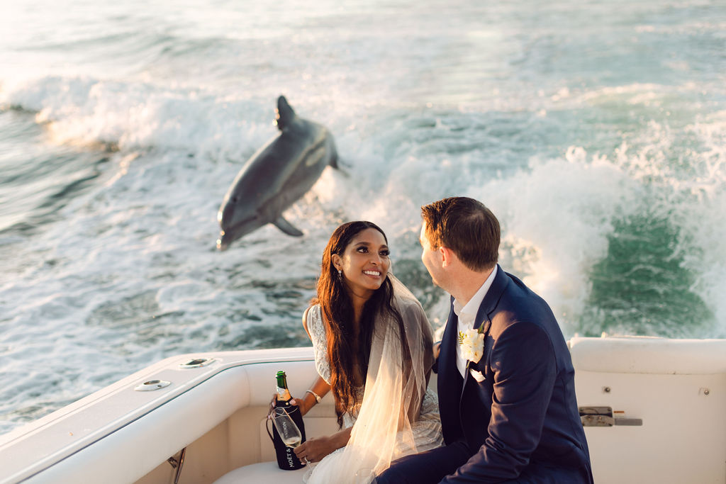 Dolphin jumps in waves behind couple at a Naples, Florida beach wedding venue.