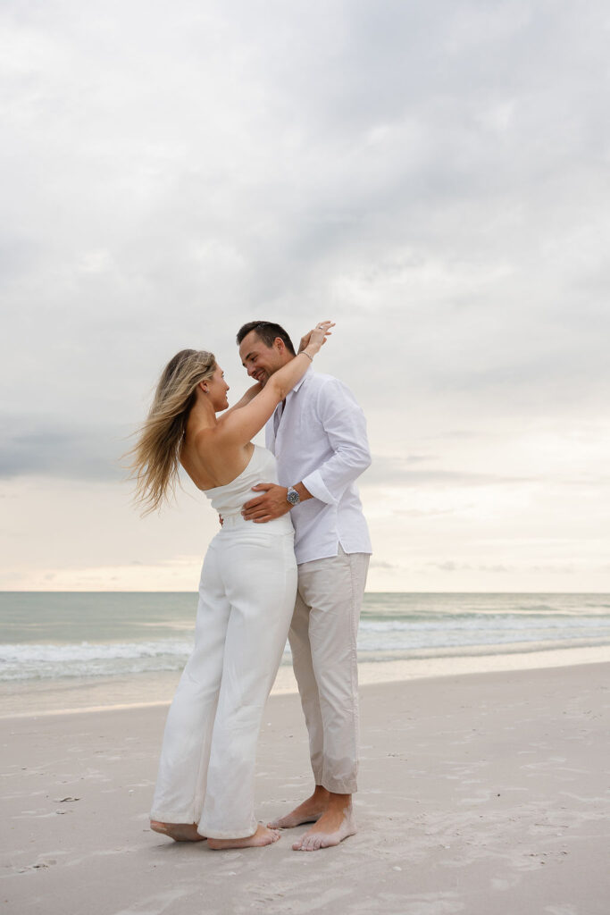 Casual beach engagement photos with couple barefoot in the sand and smiling